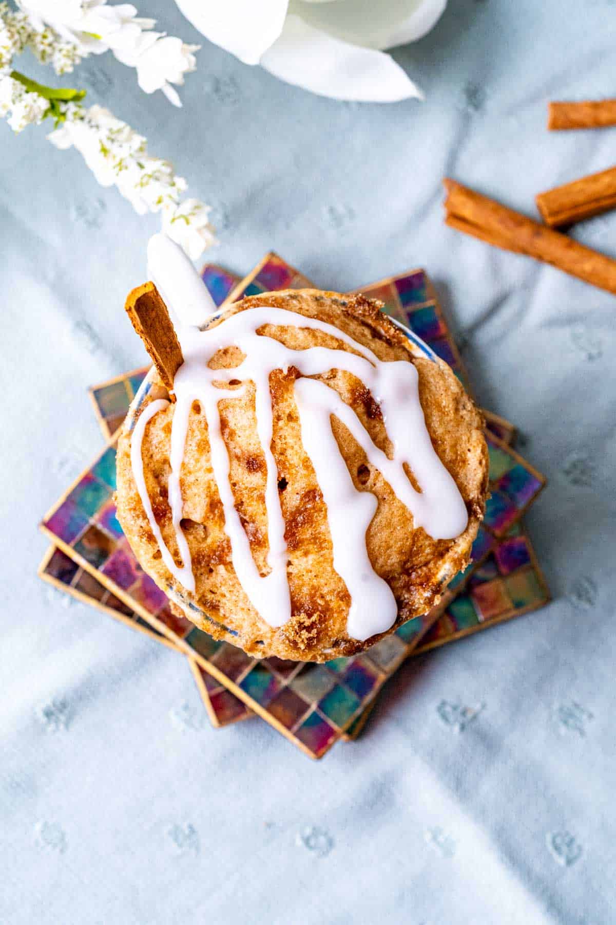 Cinnamon roll cake in a cup placed on a light blue table cloth.