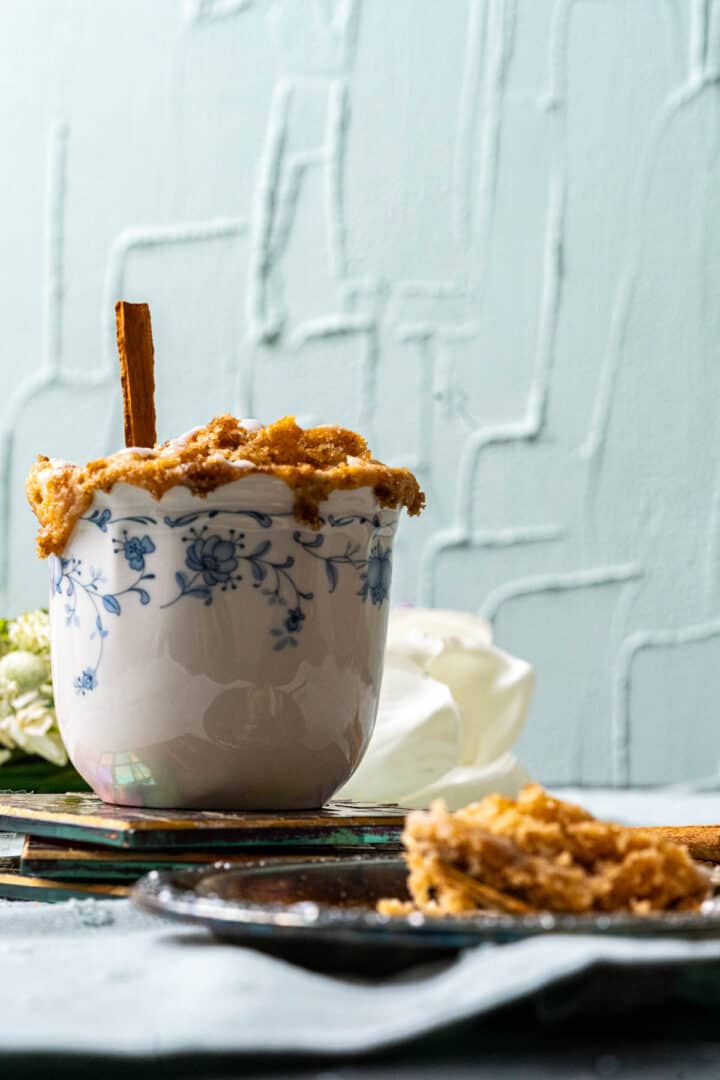 cinnamon mug roll with a cinnamon stick in a white tea cup with flowers in the backdrop.