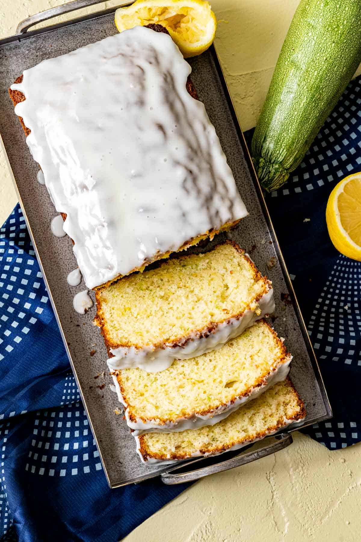 Lemon zucchini bread in a gray cake plate with zucchini and lemons sitting on the side of the plate.