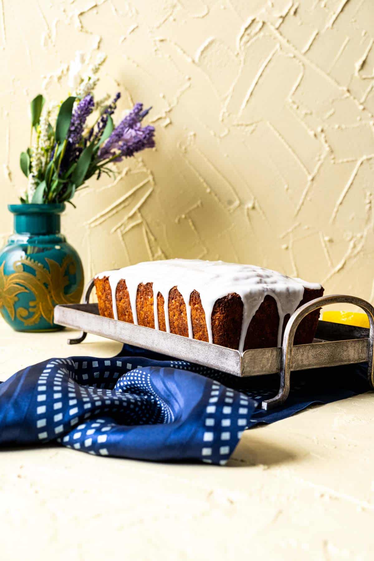 Whole loaf of lemon zucchini bread sitting on a gray tray with flowers in the backdrop.