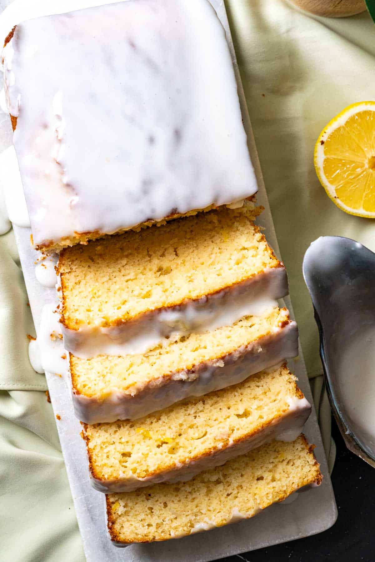 Slices of lemon bread sitting on the cake plate with lemon glaze on the side.