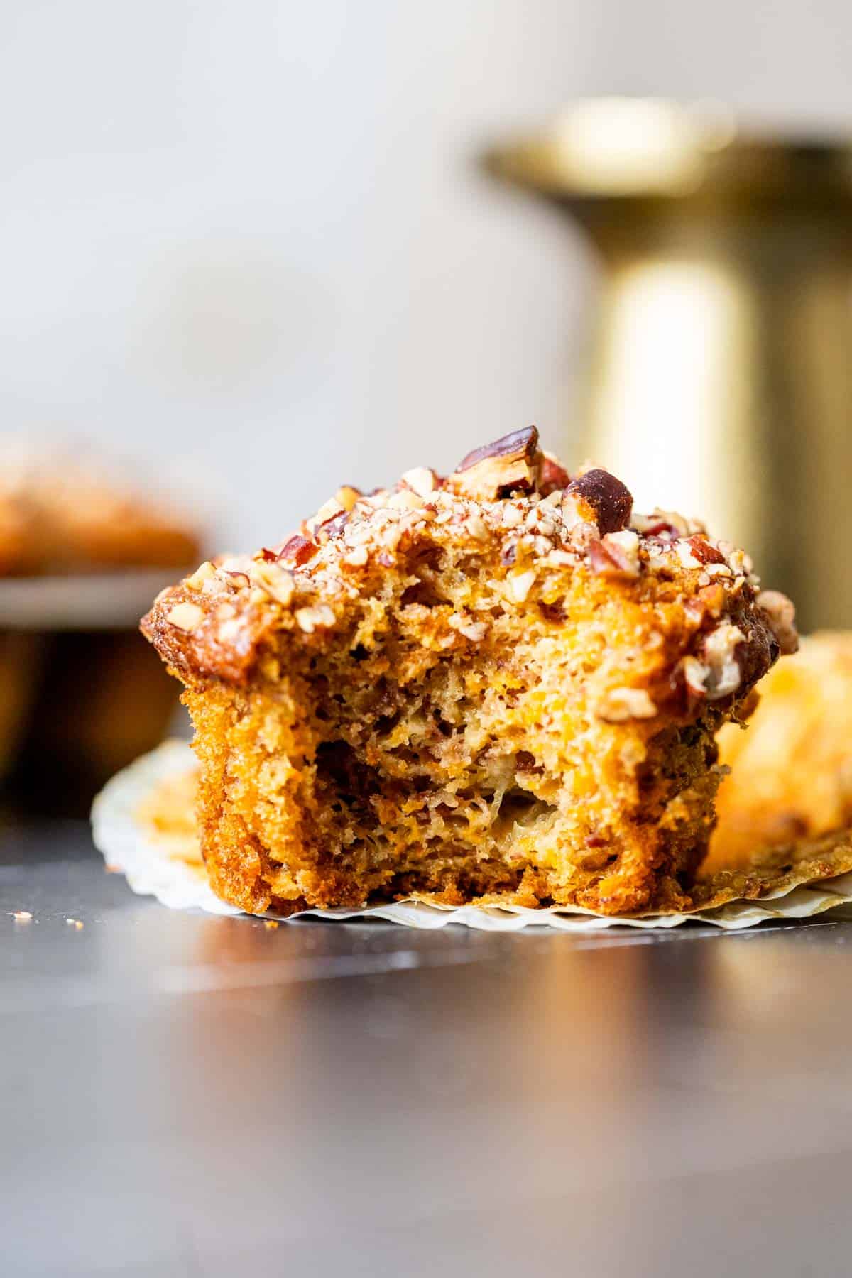 Banana carrot muffin showing the texture of the muffin sitting on a table with a golden stand in the backdrop.