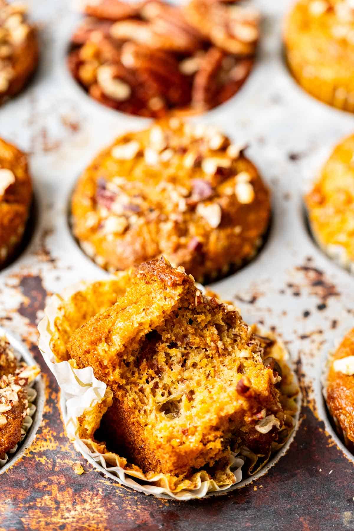 One Carrot Banana Muffin cut in half showing the texture with roasted pecans on the top in an antique silver muffin tray.