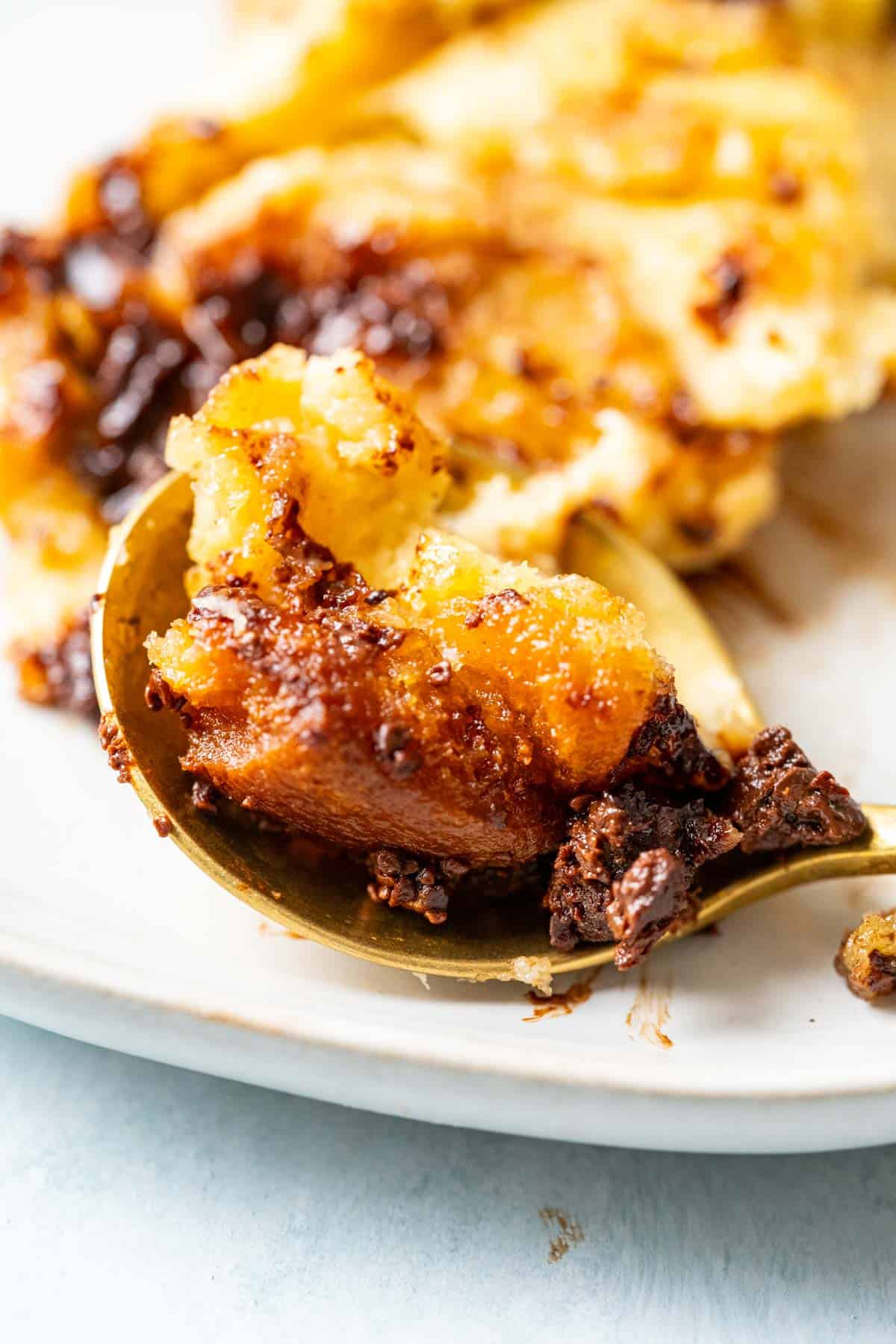 One bite of chocolate chips bread pudding served in a small white plate in a silver spoon.