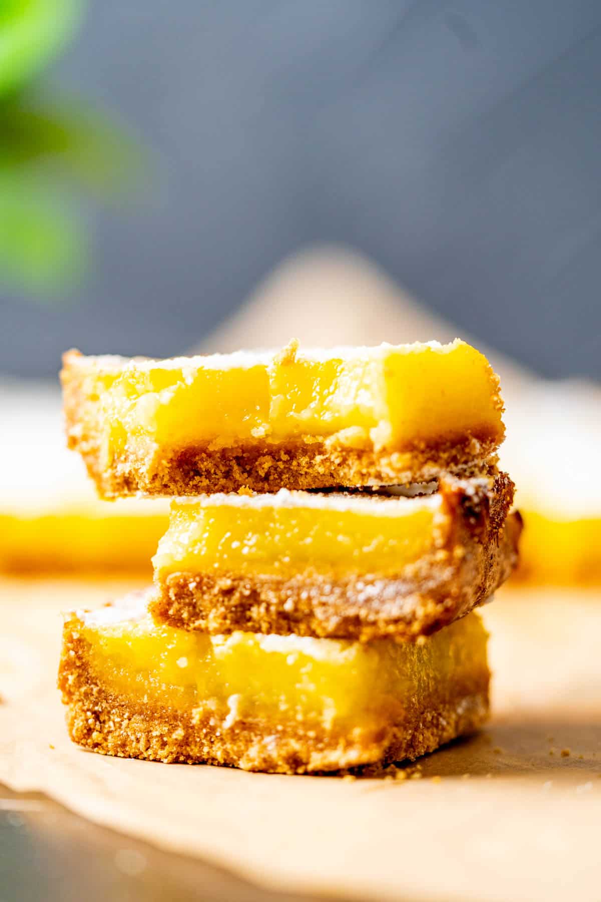 Three lemon bars with graham crust sitting on top of each other showcasing the luscious lemon curd.