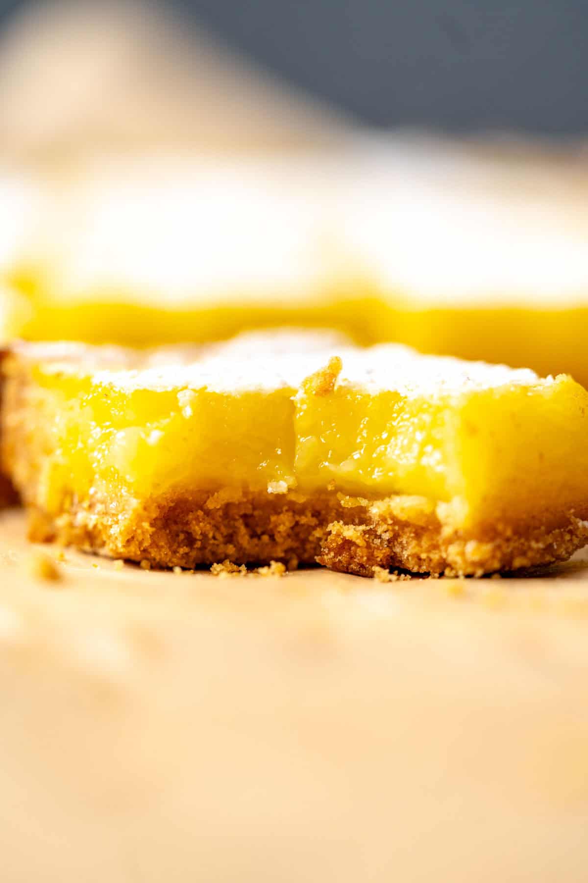 One lemon bar with lemon curd and graham cracker crust sitting on the table.